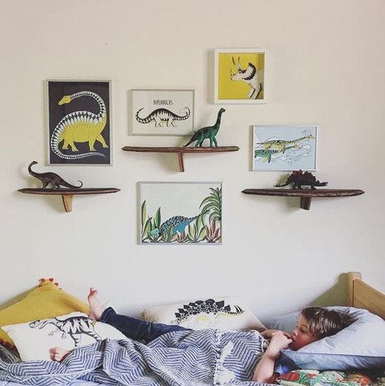 دکوراسیون اتاق کودک پسری با تم دایناسور که روی دیوار و تخت آن، تابلو و عروسک و روبالشی با طرح دایناسور قرار داده شده است
